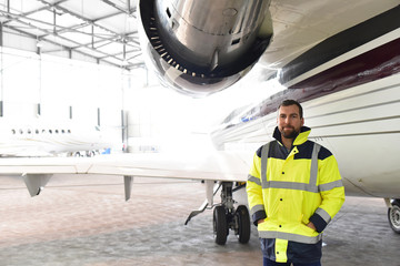 Portrait of an aircraft mechanic in a hangar with jets at the airport - Checking the aircraft for...