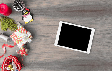 tablet display on table with isolated white screen for mockup in Christmas time. Christmas tree, gifts, decorations in background.