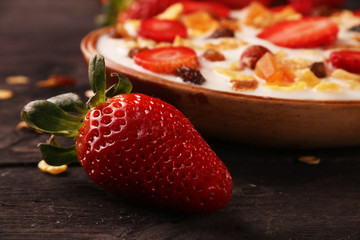Bowl of yogurt with strawberries and granola muesli, over a white wood background.