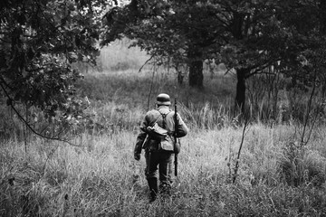 Single Re-enactor Dressed As German Wehrmacht Infantry Soldier In World War II Walking In Patrol Through Autumn Forest. WWII WW2 Times. Photo In Black And White Colors