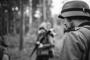 Re-enactors Dressed As World War II German Wehrmacht Soldiers Marching Walking Along Forest Road In Summer Day. Photo In Black And White Colors. Military German Soldier Of WWII Times - Powered by Adobe