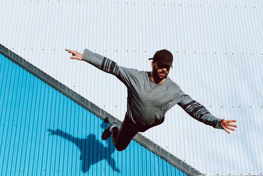 barefoot guy in stylish outfit performing flip near wall of modern building on city street