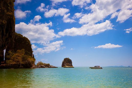 The rock in the sea is painted with gold paint. Speedboat floats nearby. Blue sky, a lot of clouds. Cave beach. Pranang, Krabi province
