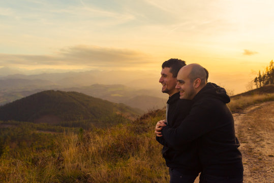 Side view of homosexual couple embracing on route in darkness and picturesque view of valley in fog