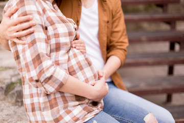 couple expecting a baby. pregnant in a plaid shirt. hands on pregnant belly