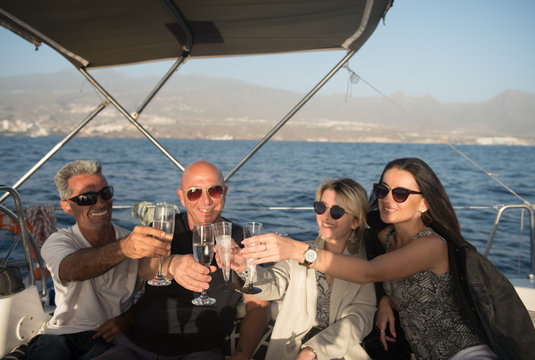 Happy males and young females in sunglasses clanging glasses of champagne and resting on expensive boat floating on water in sunny day