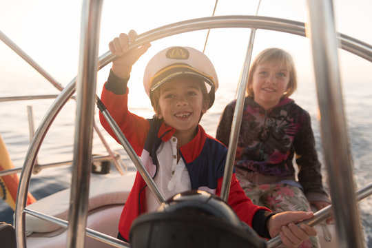 Positive kids in captain hat floating on expensive boat on sea in sunny day