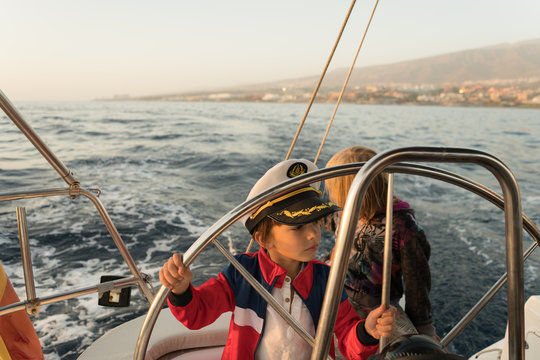 Positive kids in captain hat floating on expensive boat on sea in sunny day