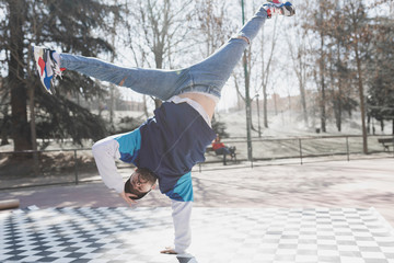 Young athletic guy practicing break dance in park in sunny weather
