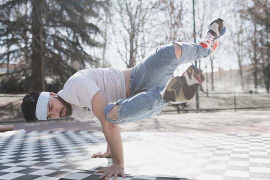 Young athletic guy practicing break dance in park in sunny weather