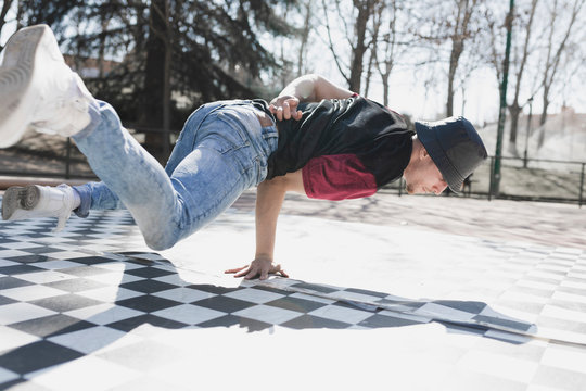 Young athletic guy practicing break dance in park in sunny weather