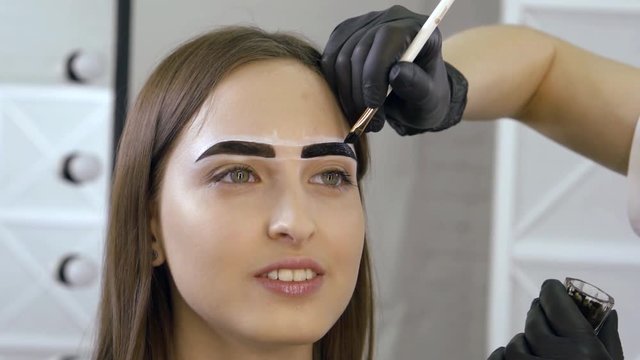 smiling young woman with green eyes is sitting in beauty salon during brows coloring process