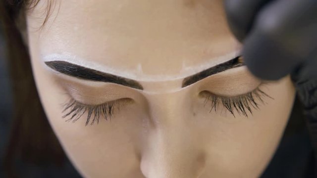 close-up view of brows of young female model during painting process in beauty salon