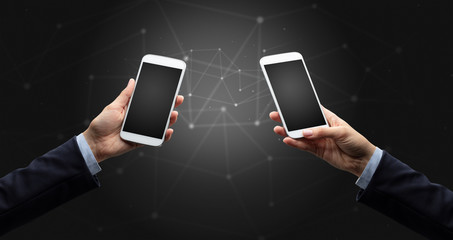 Close up of two hands holding smartphones to each other, wireless connection concept