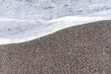 White Foam of Surf on a Black Volcanic Sand Beach in Sicily
