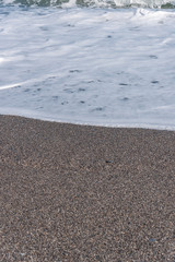 Fototapeta na wymiar White Foam of Surf on a Black Volcanic Sand Beach in Sicily