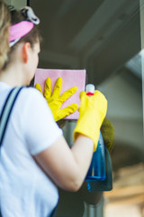 Young woman washing windows with yellow rubber gloves, cloth and cleaning product. 