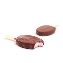 Bitten ice cream popsicle on a stick in chocolate on a yellow background