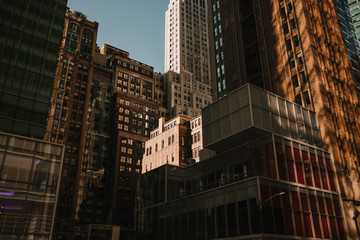 From below of exterior of buildings in density on street of New York city in sunlight