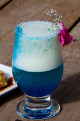 blue cocktail with snack on a plate. on a wooden table in a glass blue cocktail with foam. and there is a plate with a snack