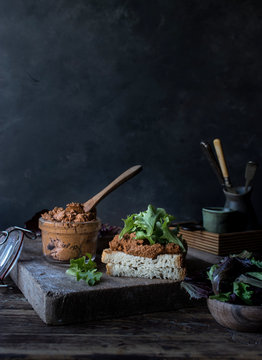 Sandwich of pate of dry tomatoes, fresh salad and cabbage on tray near knife on wooden board on black background