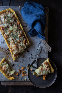 From above slice of tart with pumpkin and Emmental cheese on dish with fork placed on tray on wooden background