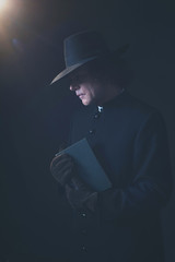 Mysterious victorian priest in hat holding book.