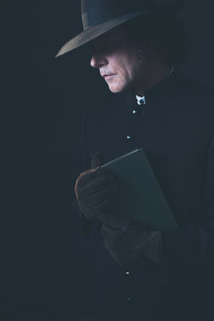 Mysterious victorian priest in hat holding book.