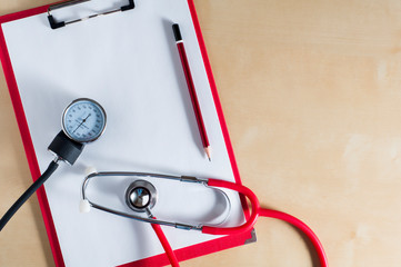 Red stethoscope, tonometer and red pencil on a red clipboard. Top view. Right copy space. Medical...