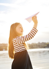 Cute little girl plays with paper airplane on the beach.