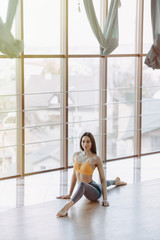Fototapeta premium young attractive girl doing fitness exercises with yoga on the floor against the background of panoramic windows