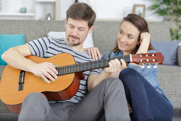 happy relaxed couple with guitar sitting on couch at home