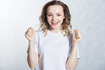 Portrait of overjoyed beautiful woman clenches fists with happiness, poses against white background.