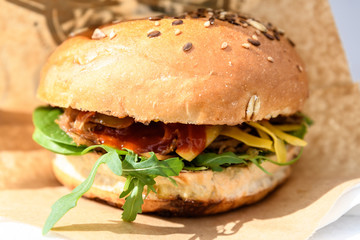 Close up of a fresh burger with pulled meat, cheese and fresh arugula leaves in a fresh bun with seeds, on brown paper for sale at a street food festival