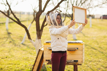 A young beekeeper girl is working with bees and beehives on the apiary, on spring day