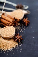 Brown cane sugar, cinnamon sticks and star anise closeup on black board background.