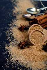 Brown cane sugar, cinnamon sticks and star anise closeup on black board background.