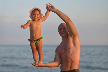 Dad holds his little daughter on one hand in the summer at sea.