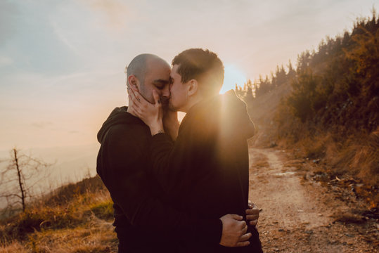 Side view of homosexual couple hugging and kissing on path in forest in sunny day