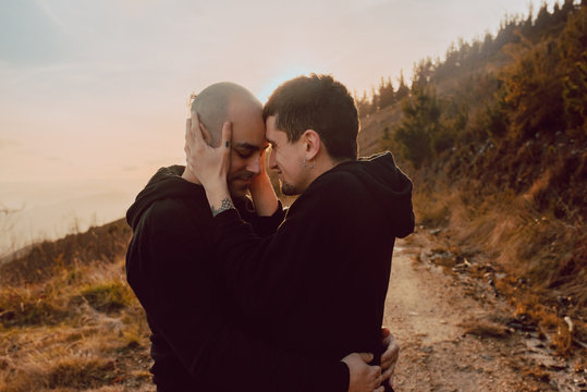 Side view of homosexual couple hugging and kissing on path in forest in sunny day