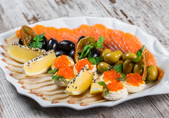 Seafood platter with salmon slice, quail eggs with red caviar, slices fish fillet, decorated with olives and lemon in plate over rustic background. Mediterranean appetizers
