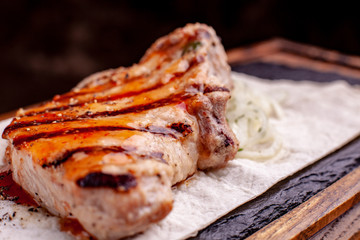 Grilled steak with french fries and vegetables served on black stone on wooden table with red sauce
