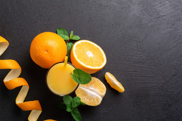A group of oranges and a glass of juice on a dark background.
