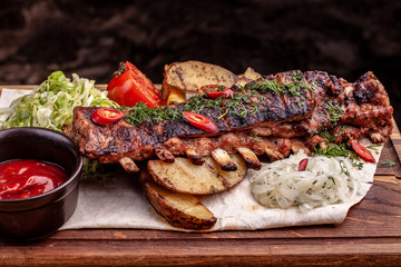 Delicious barbecued ribs seasoned with fresh herbs, cabbage salad, backed potato on an old rustic wooden chopping board