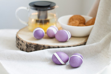 Fototapeta na wymiar lilac Easter eggs on wooden stand with tea and cookies