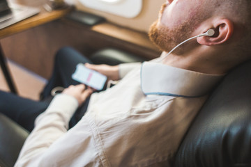 Young attractive and successful businessman is resting and listening to music works while sitting in the chair of his private business plane