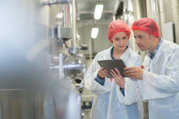 two quality control workers wearing hairnets looking at digital tablet