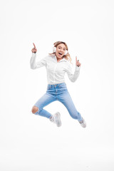 Gorgeous redhead lady listening music hits on radio in headphones and jumping high. Charming girl in in casual clothes and earphones dancing with hair waving on white background. Full-length portrait