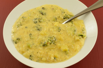 Broccoli and potato cheese chowder soup in white bowl with spoon in red background