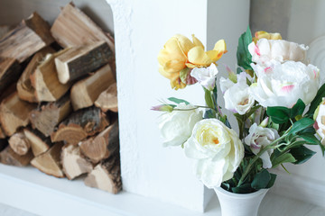 Beautiful white and yellow spring flowers on the background of the fireplace, firewood in the fireplace.